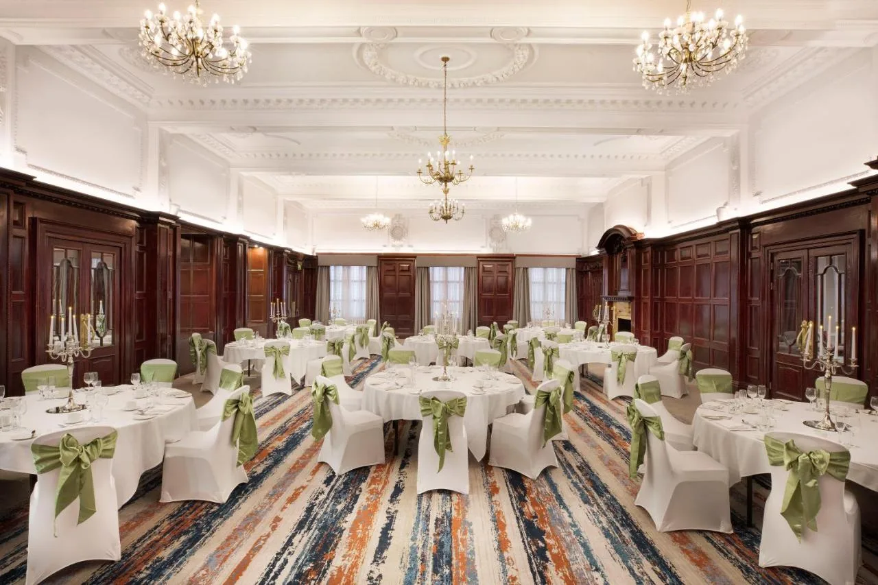 a ballroom with white tables and chairs and chandeliers at Leonardo Hotel Cardiff in Cardiff